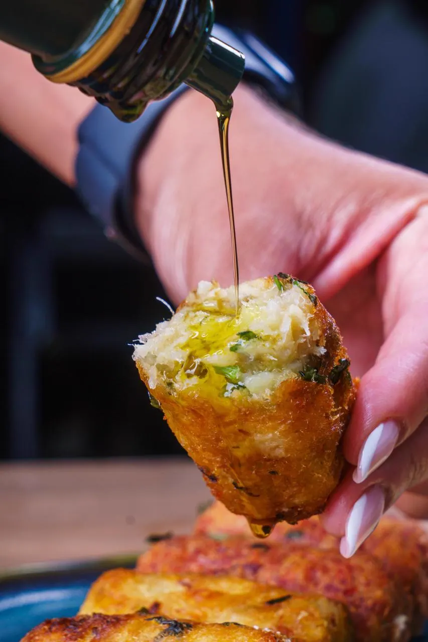 Bolinho de bacalhau aberto, com fio de azeite sendo servido por cima