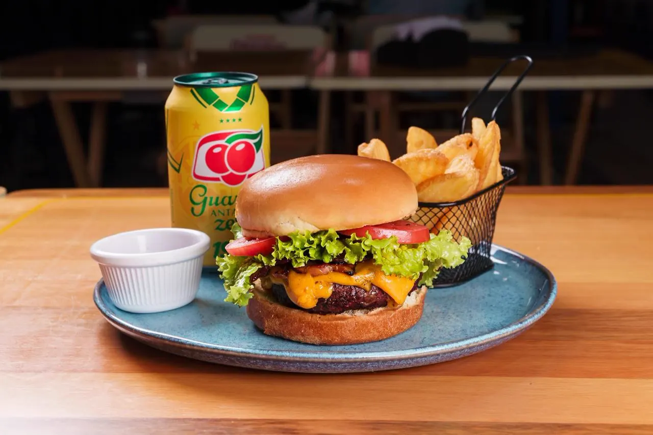Hambúrguer com cheddar e fritas em cesta, num prato azul, com guaraná em lata