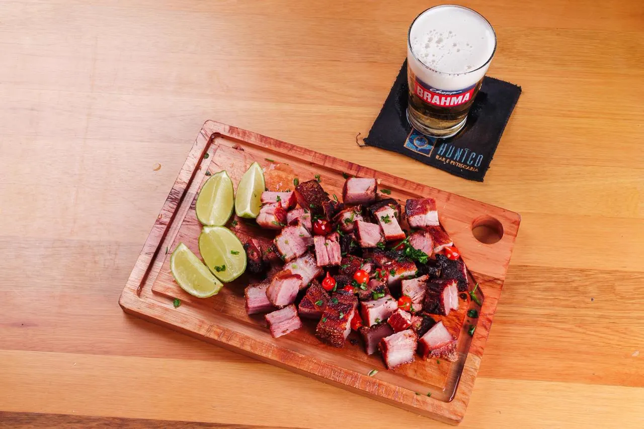 Torresmo em cubos com limão e pimenta, na tábua, vista de cima, com chopp Brahma ao lado